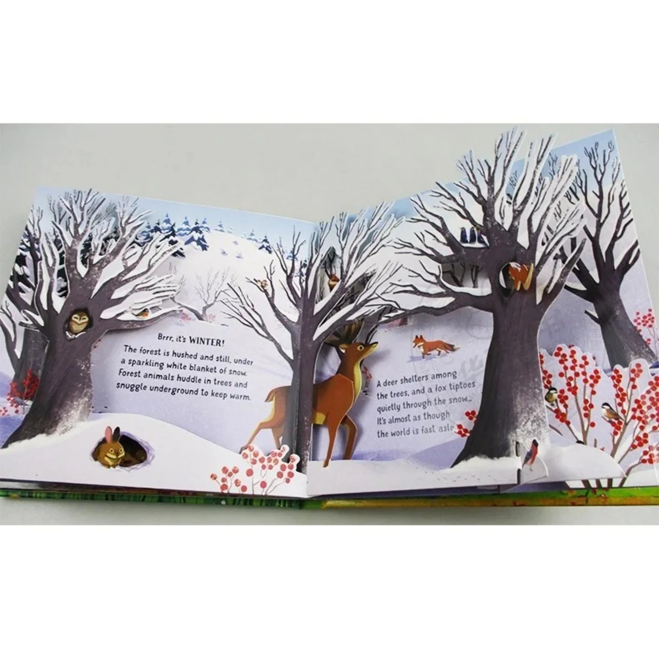 Illustrated book open to a winter scene with trees and animals